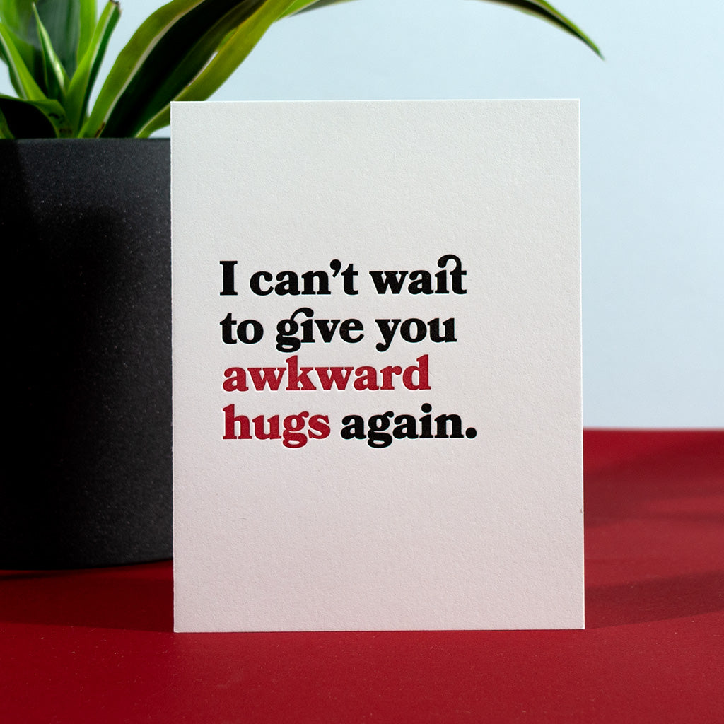 Greeting card with black and red text letterpress printed on white paper. I can't wait to give you awkward hugs again.