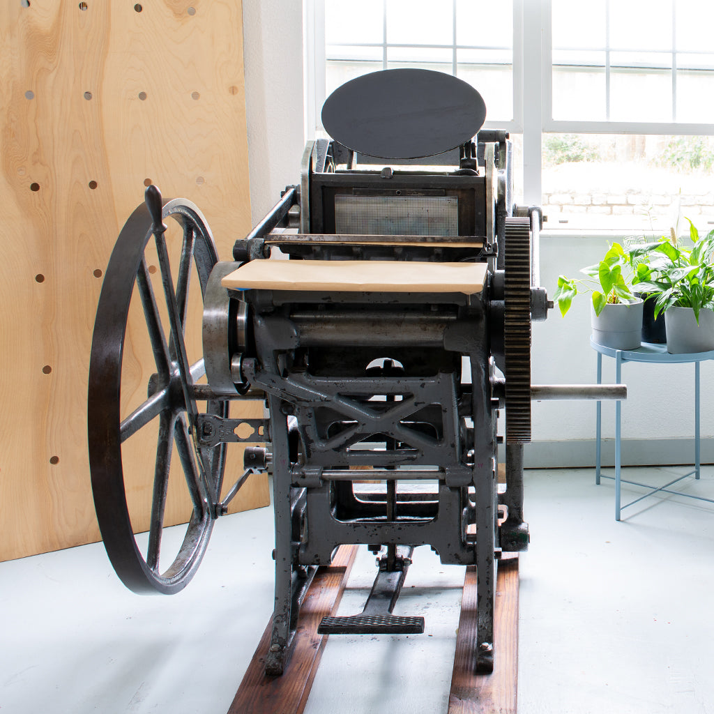 Petunia, an antique printing press with a treadle, in a brightly lit room with house plants and open windows.